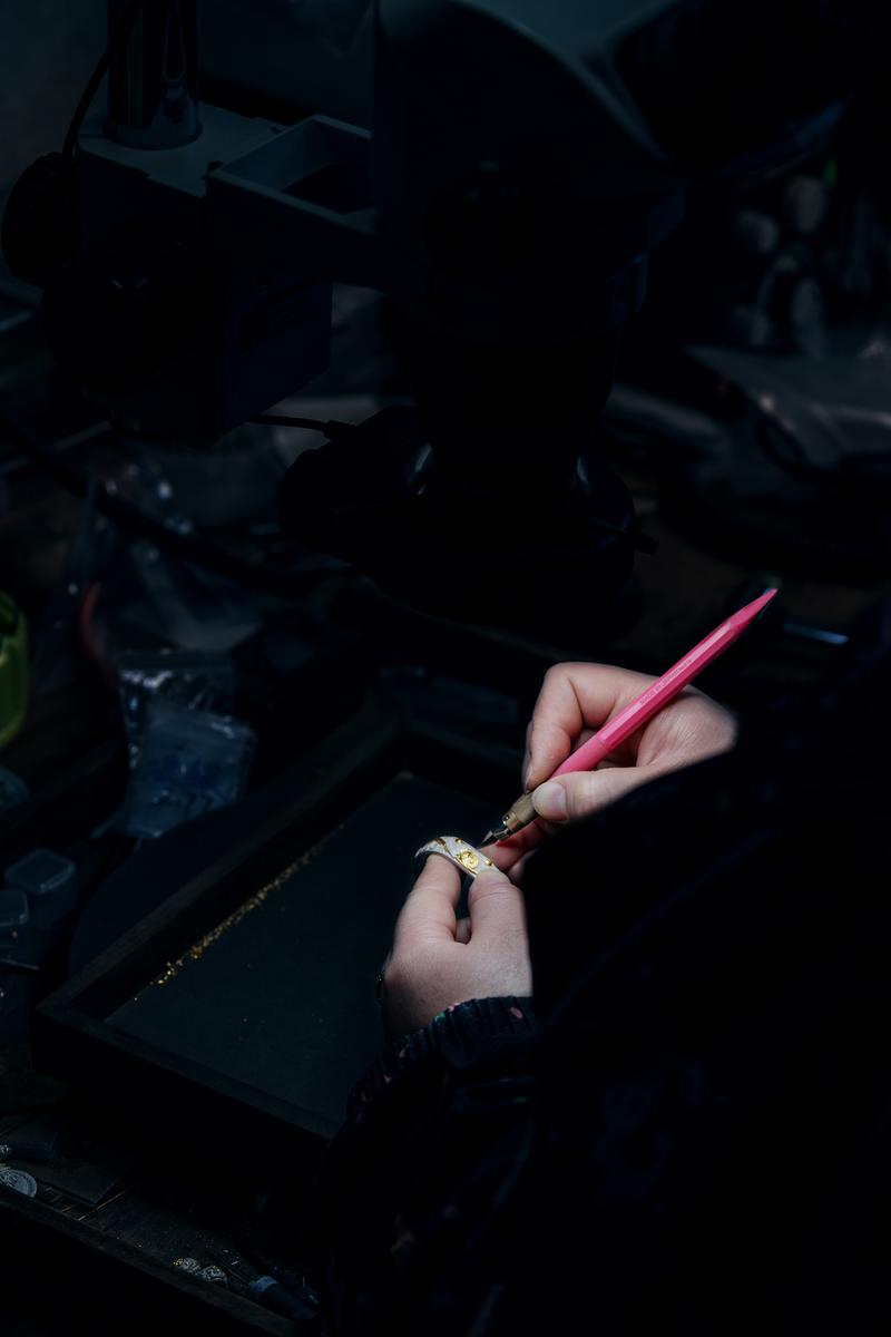 A silversmith engraving a fire-gilded silver ring under a stereo microscope