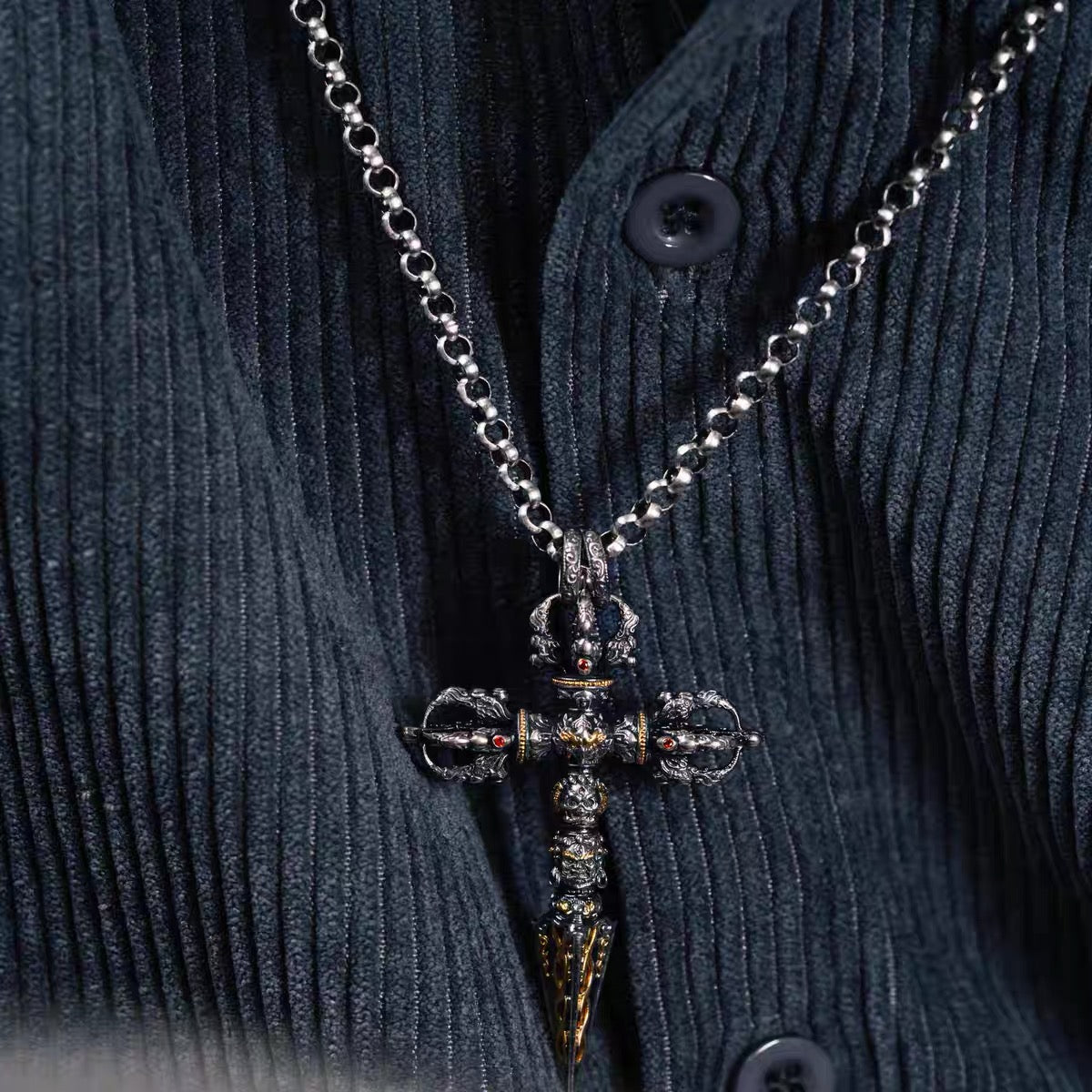 24K fire-gilded phurba pendant worn on a silver chain over a dark corduroy shirt