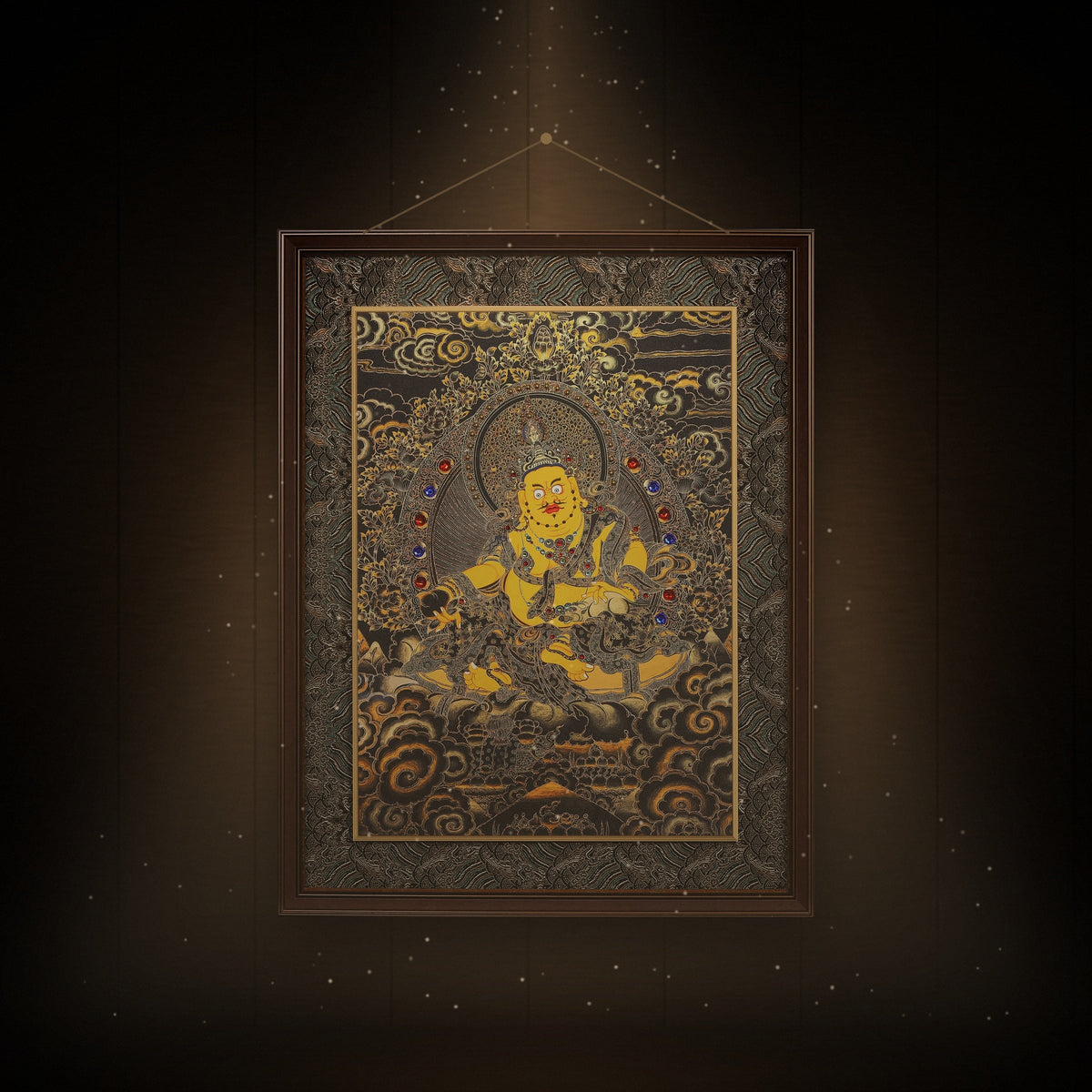 Yellow Jambhala black and gold thangka hanging in a room under warm light