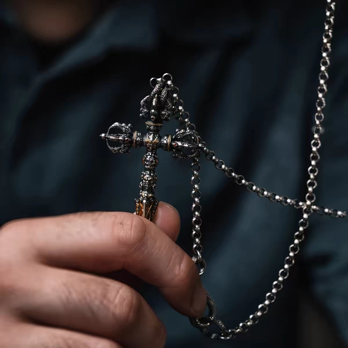 Fire-gilded phurba pendant held in the hand for scale, with its silver chain and carved S-hook clasp