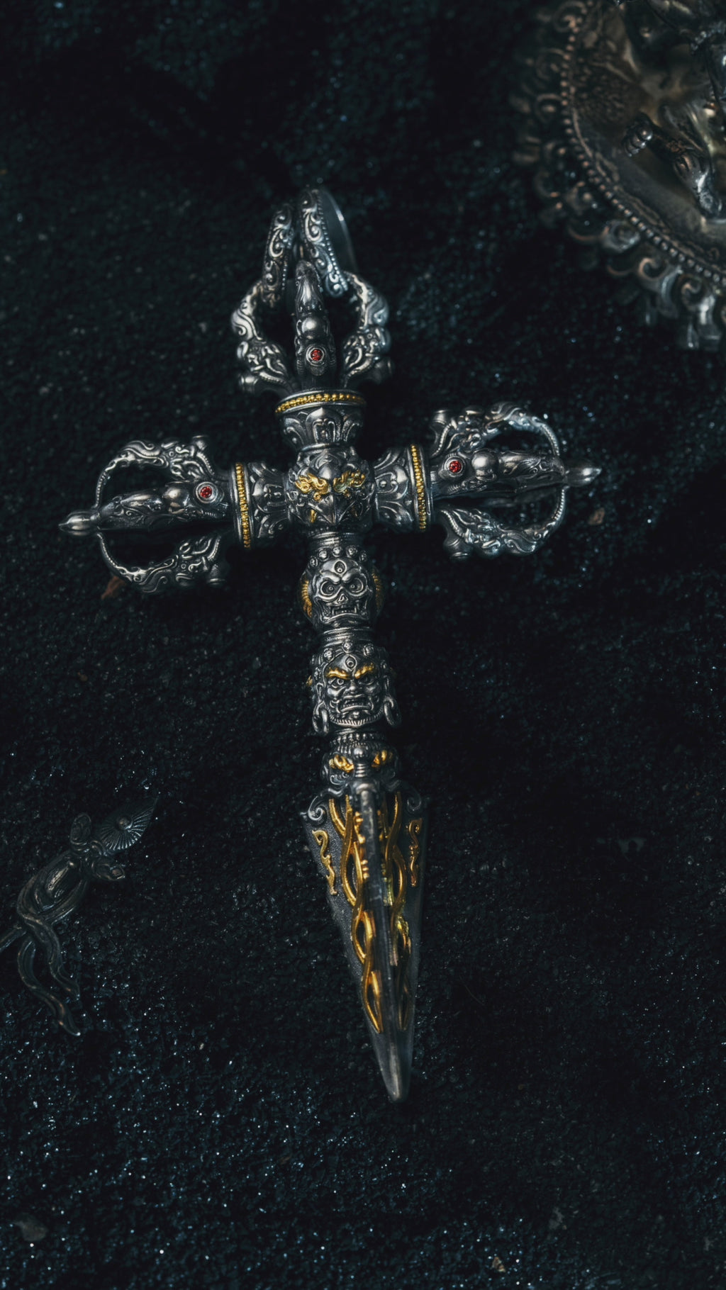 Phurba pendant turning in the light, three wrathful heads stacked above the serpent-carved blade