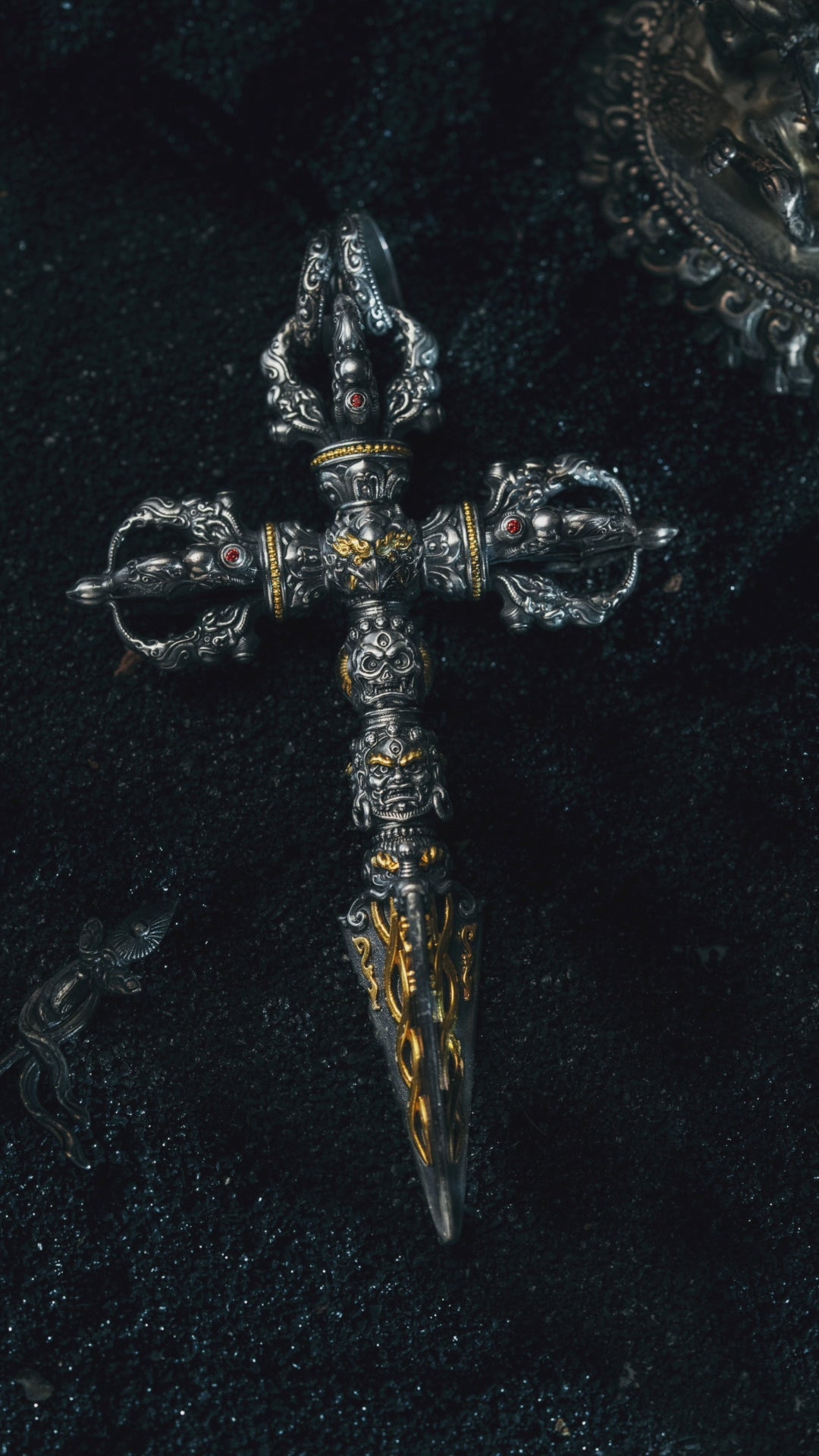 Phurba pendant turning in the light, three wrathful heads stacked above the serpent-carved blade
